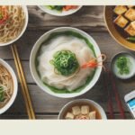 Flat-lay of gluten-free Chinese dishes including rice noodles, tofu stir-fry, steamed vegetables, and congee, with chopsticks and a gluten-free soy sauce bottle on a wooden table.